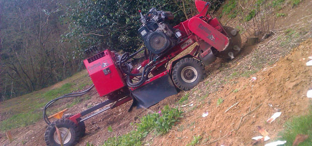 Red stump grinder situated on steep hill